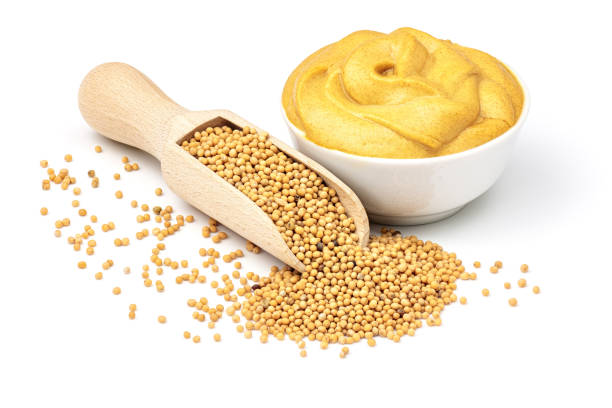 Mustard seeds in the wooden scoop and mustard sauce in a bow.